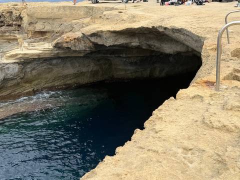 Rocky coastal cave opening with dark blue water at the Blue Grotto area