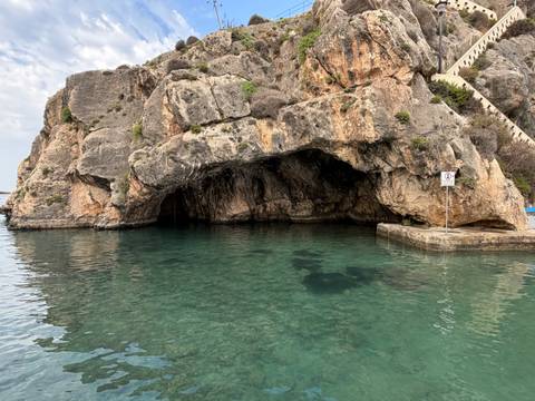 Turquoise seawater at the entrance of a large coastal cave with rugged rock walls