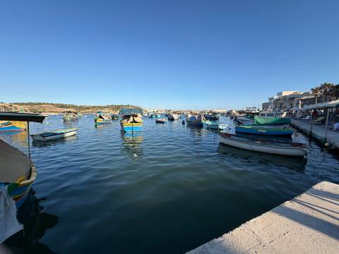 Colorful traditional fishing boats moored in a calm Maltese harbour under clear sky