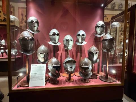 Museum display of medieval helmets arranged in glass cases with information card