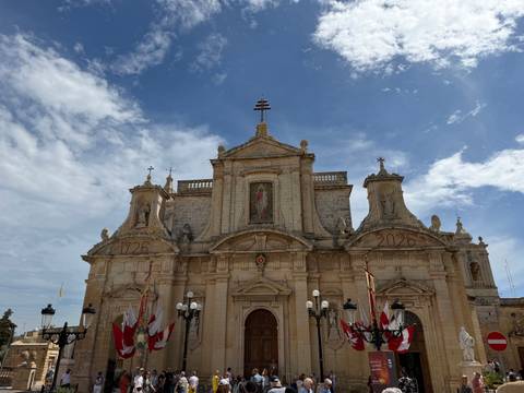 Baroque church facade decorated with flags and blue sky with scattered clouds