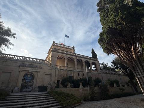 Historic villa with arcaded balcony, EU flag flying, surrounded by tall trees