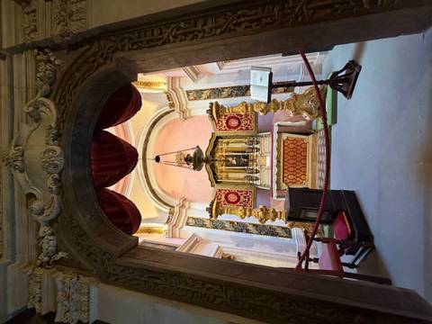 Lavish ornate altar inside a historic chapel with gold candlesticks and red drapery