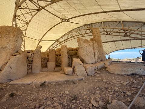 Megalithic temple ruins protected under a large white canopy with a visitor photographing