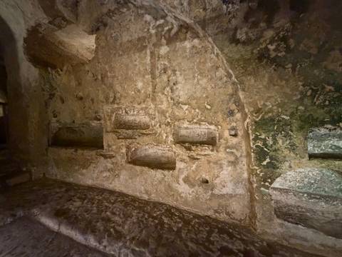 Rough-textured stone wall with several carved tomb niches inside an ancient underground catacomb.