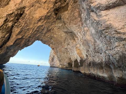 Sea cave arch of golden limestone towering over clear blue Mediterranean water, viewed from a boat.