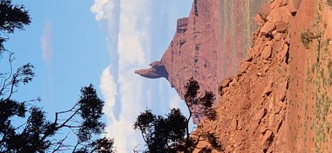 Isolated sandstone spire rising from red desert terrain in Monument Valley under blue sky.