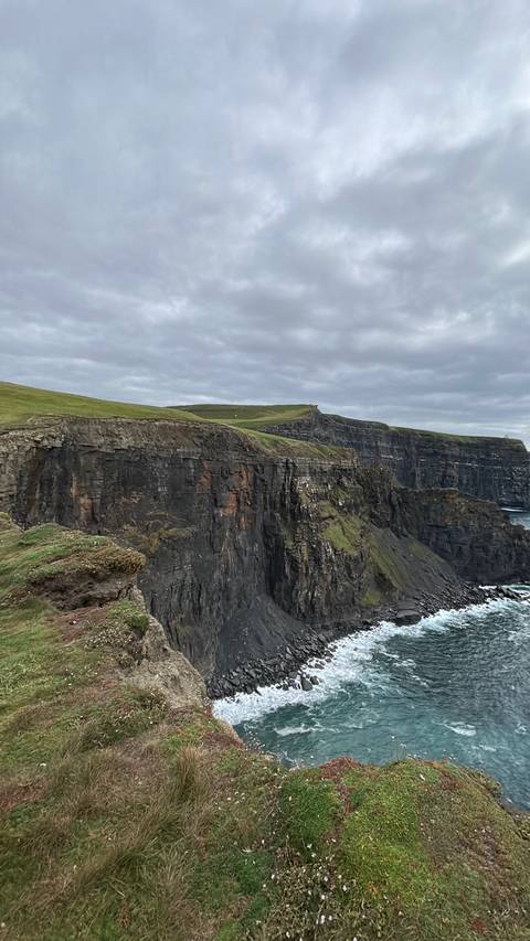 Dramatic sheer cliffs plunging into the Atlantic Ocean at the Cliffs of Moher under overcast skies.
