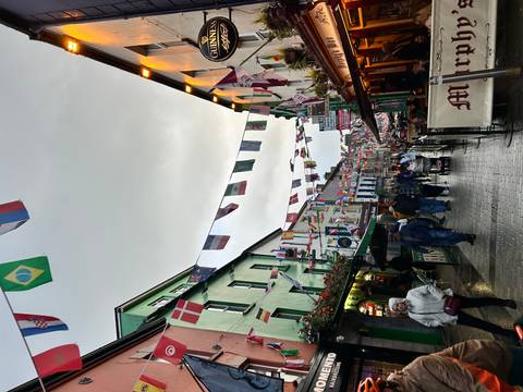 Colorful pedestrian street lined with Irish pubs and shops, festooned with international flags on a damp evening