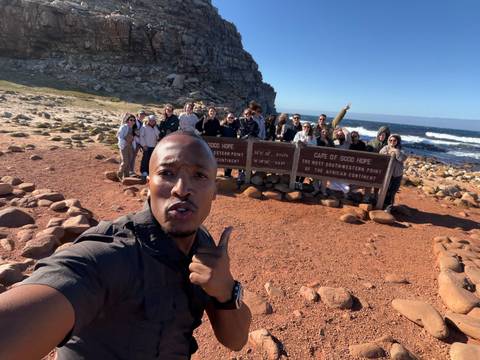Excited tour group taking a selfie at Cape of Good Hope sign on a sunny coastal day