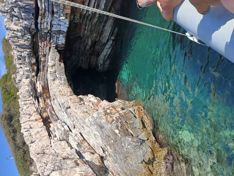Clear turquoise water at the entrance of a rocky coastal cave seen from a small boat.