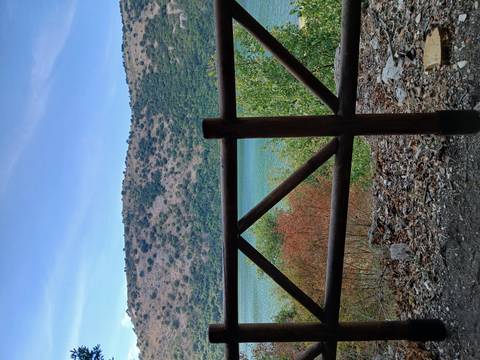 View across wooden railing toward blue-green mountain lake and dry hillside vegetation.