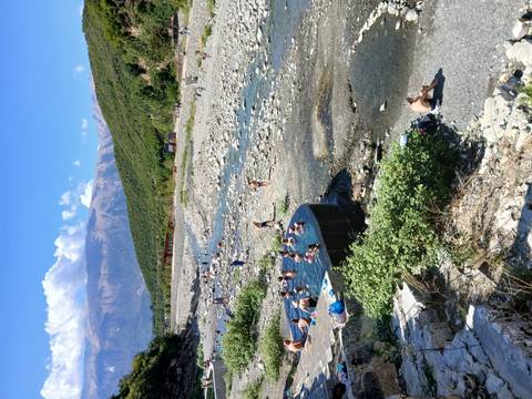 Natural hot springs pools beside a rocky river valley with bathers and mountains in background.