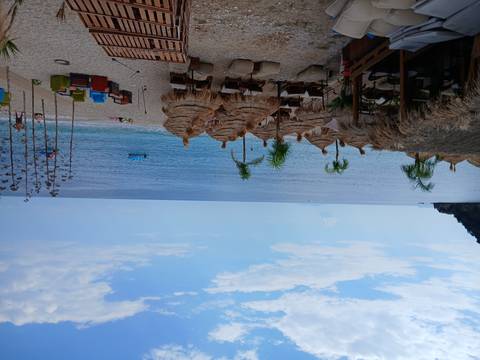 Sandy beach with thatched umbrellas, loungers and a beach bar facing calm blue waters.