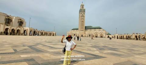 Traveler posing and waving in the vast courtyard of Hassan II Mosque in Casablanca with date text overlay.