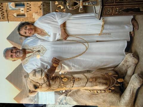 Elegantly dressed couple standing beside a decorated camel with the pyramids towering behind at golden hour