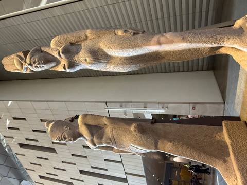 Two colossal ancient statues displayed inside a modern museum hall lit by skylights
