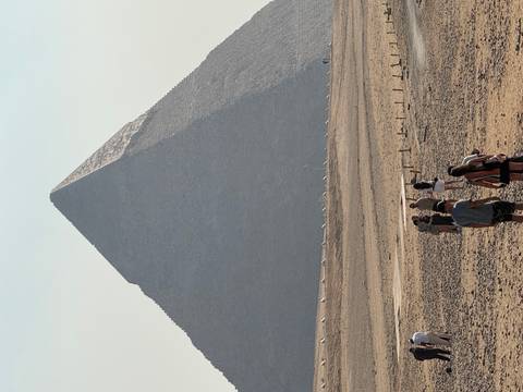 Tourists walking toward the massive pyramid rising from the desert plateau on a hazy day
