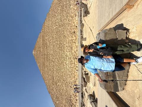 Travelling couple standing in front of the towering blocks of the Great Pyramid on a sunny day