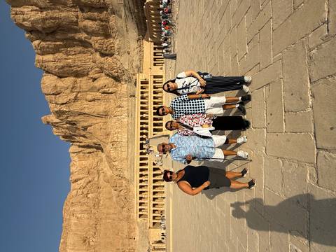 A group of travelers pose in front of Hatshepsut’s mortuary temple with towering cliffs behind.