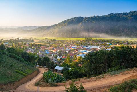 Early-morning mist hangs over a valley town surrounded by lush green mountains in northern Laos.