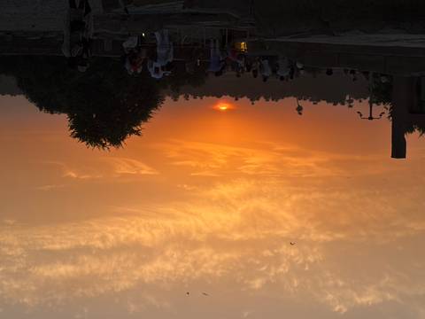 Crowds watch a fiery orange sunset with silhouettes of palm trees and distant minarets on the Nile.