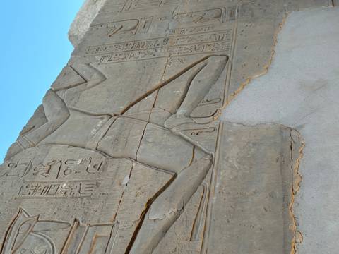 Close-up of ancient Egyptian relief carving showing a kneeling figure with hieroglyphs.