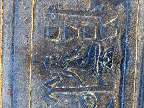 Close-up of a single figure carved into dark temple stone showing mythological scene.