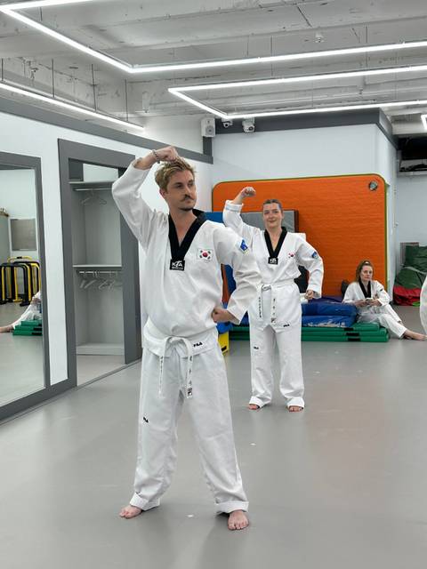 Participants dressed in white doboks practicing Taekwondo forms in a training hall