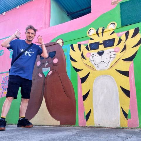 Traveller posing playfully beside a bright cartoon mural of a bear and tiger
