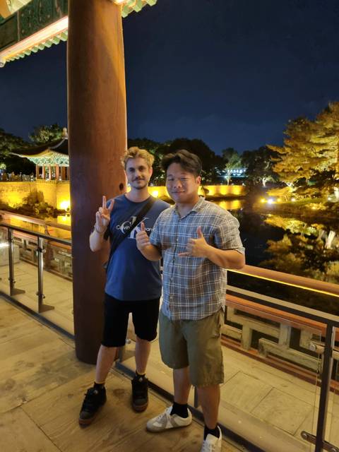 Two friends making peace signs by a softly lit pond and traditional pavilion at night