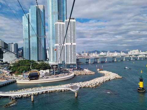 Cable car gliding above Busan coastline with high-rise towers and bridge spanning the bay