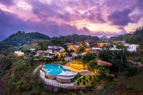 Hillside eco-resort with illuminated pool and villas nestled in lush mountains under a purple sunset sky.