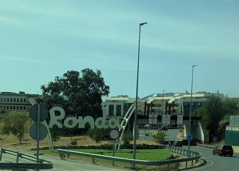 View through a bus window of a roadside sign reading 'Ronda' with modern buildings in the background.