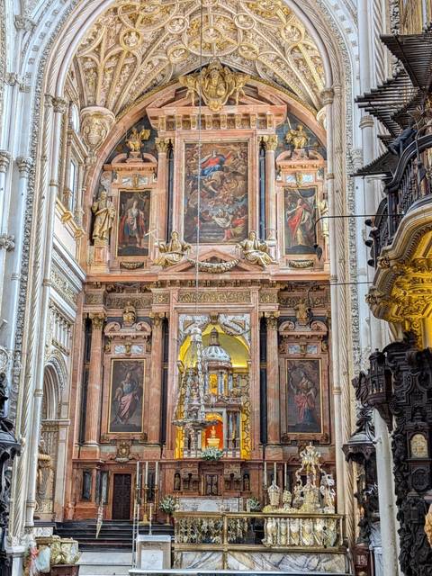 An ornate marble and gilded altar inside a grand Spanish cathedral, richly decorated with religious paintings and statues.