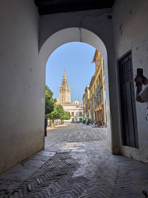 View through a white archway to Seville’s Giralda bell tower rising above a quiet cobbled street lined with historic buildings.