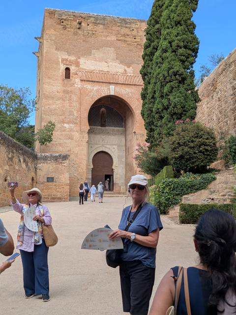 Visitors gather outside a massive Moorish stone gate within the Alhambra complex, surrounded by ancient walls and greenery.