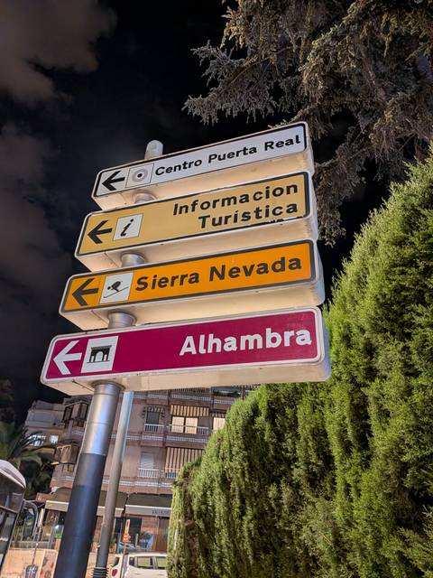Night-time close-up of colorful directional signs pointing to tourist information, Sierra Nevada and the Alhambra.