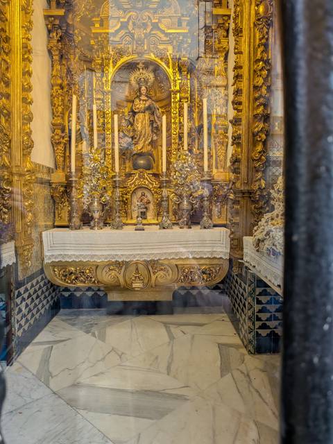 A small golden chapel with intricate altarpieces seen through protective glass inside a church.