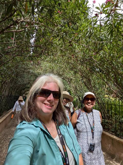 Smiling travellers take a selfie while walking under a leafy tunnel of intertwined branches.
