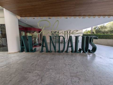 Large green 3-D sign reading 'Palace Al Andalus' outside a modern hotel entrance.