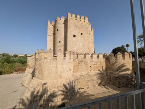 The medieval Calahorra Tower and stone ramparts stand beside the Guadalquivir River under a clear sky in Córdoba.