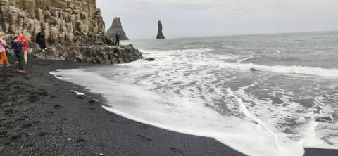 Foamy waves wash over the black sand of Reynisfjara as basalt columns and distant sea stacks frame the scene.