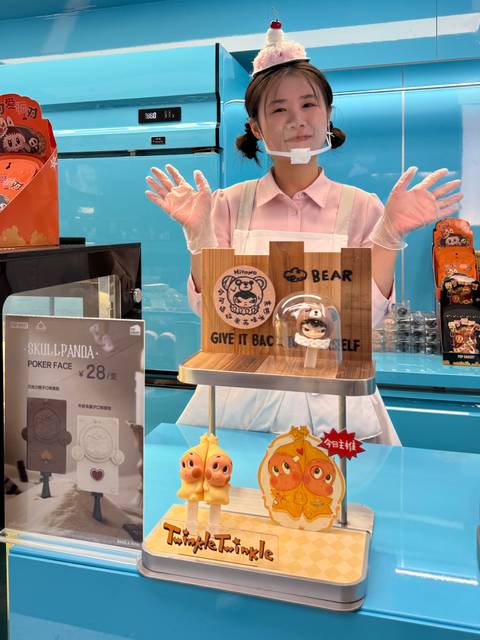 A shop attendant wearing gloves stands behind a playful cartoon-themed dessert display with Chinese signage.