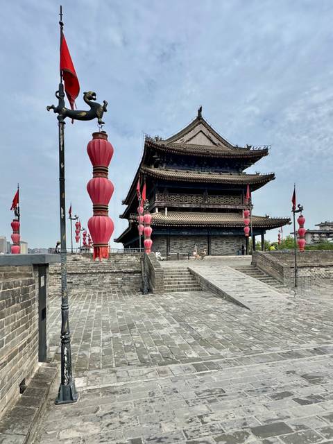Historic Chinese gate tower with rows of large red lanterns lining a stone walkway on a sunny day.