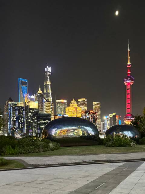 Nighttime view of Shanghai’s illuminated skyline featuring the Oriental Pearl Tower and mirrored sculptures in the foreground.