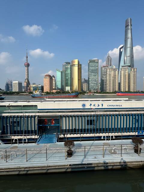Riverfront view of Shanghai’s skyline with a cargo vessel and a floating dock marked CHINAMSA in the foreground.
