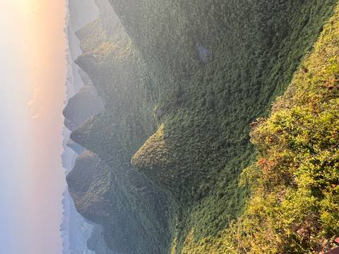 Sweeping golden-hour vista of green karst mountains and valleys stretching into the hazy distance.
