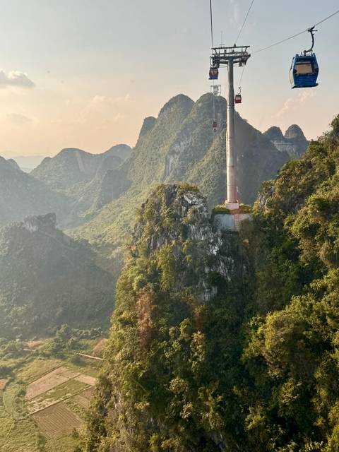 Karst mountain ridge with a tall communications tower perched on a rocky outcrop bathed in warm light.