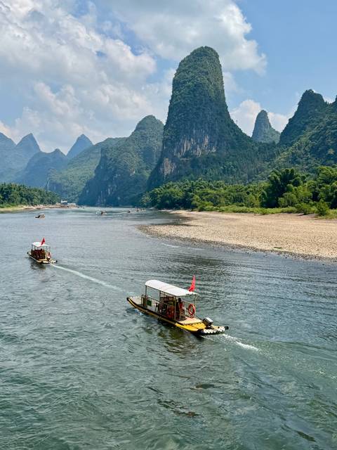 Small tour boats glide along the Li River bordered by lush bamboo and towering limestone cliffs.